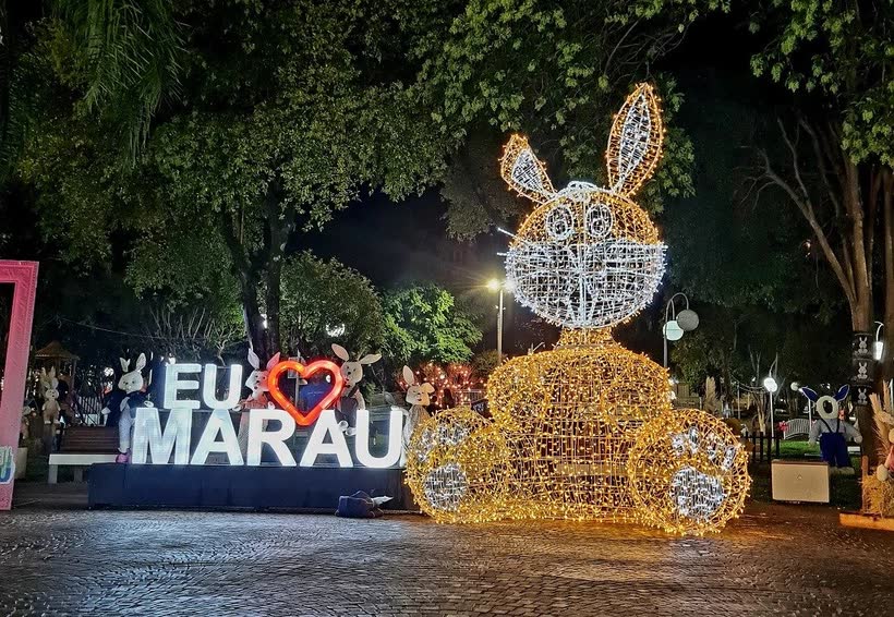 Decoração de Páscoa iluminada à noite, com coelho de luz e o letreiro Eu amo Marau