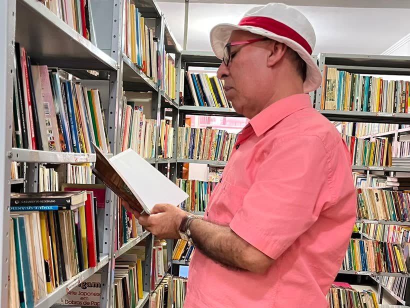 Leitor folheando um livro entre as estantes da Biblioteca Pública Municipal
