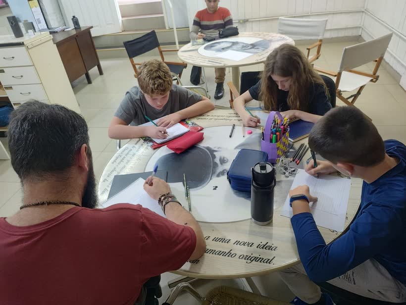Jovens desenhando ao redor de uma mesa em oficina cultural da AMAC